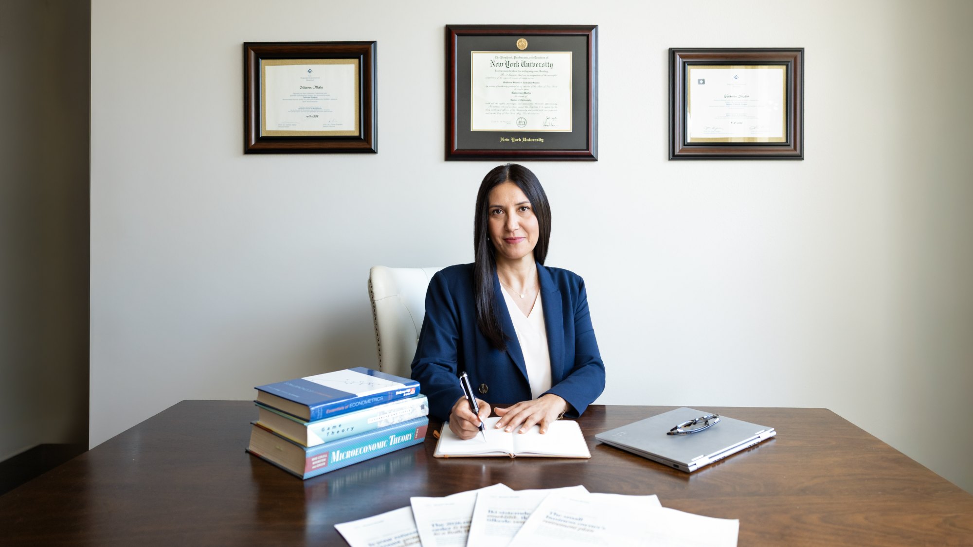 Dr. G at her desk, her diplomas on the wall behind her
