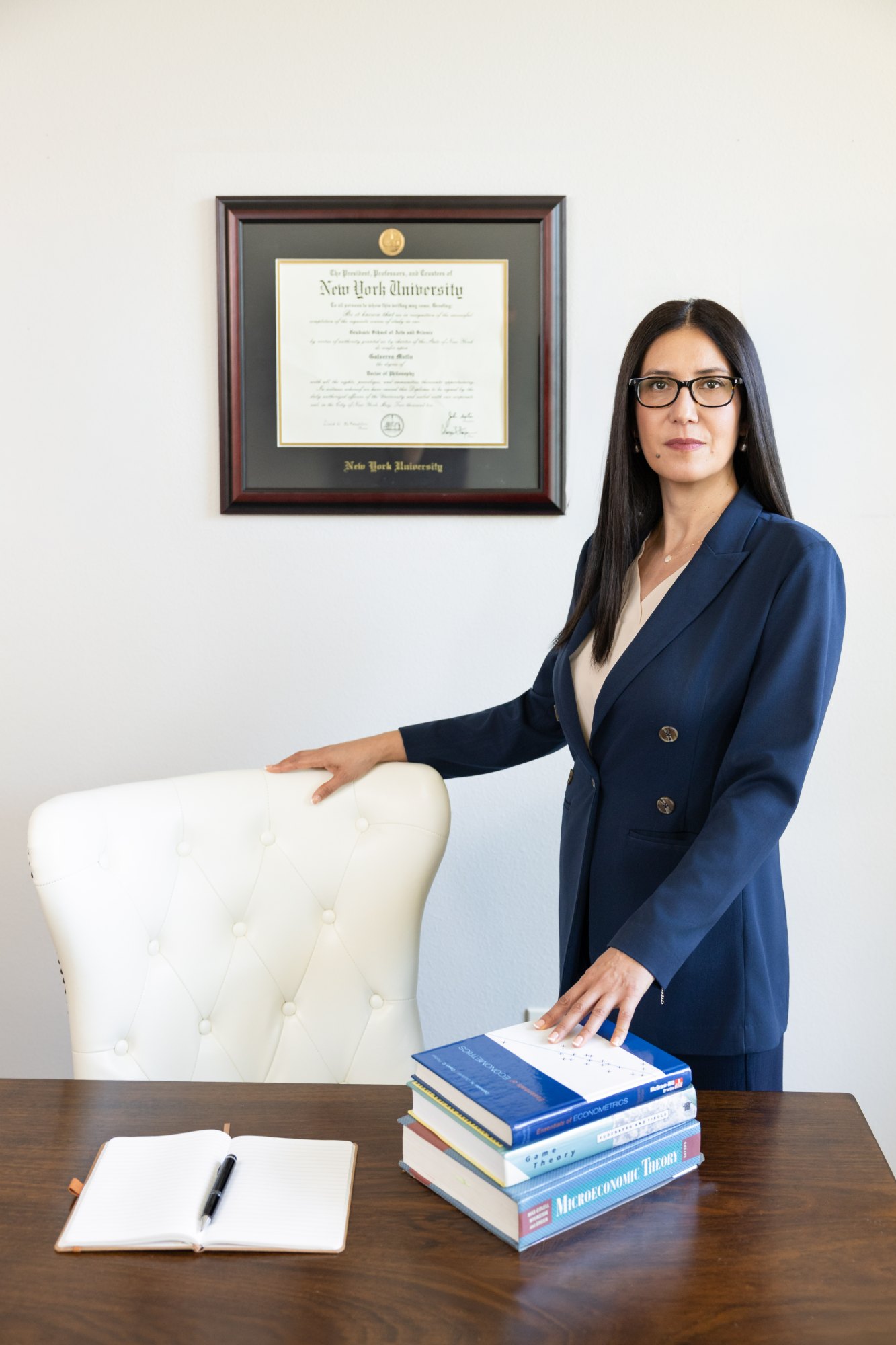 Dr. G standing at her desk, her NYU Ph.D. diploma on the wall behind her
